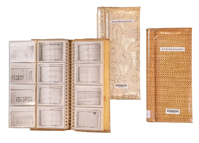 A binder filled with plastic slots containing documents and two closed wrapped booklets beside it.